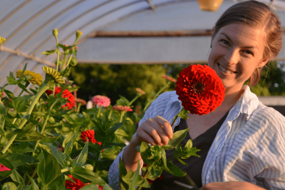 anna merkt smiles in a headshot with cherry red zinnia flower as big as her face